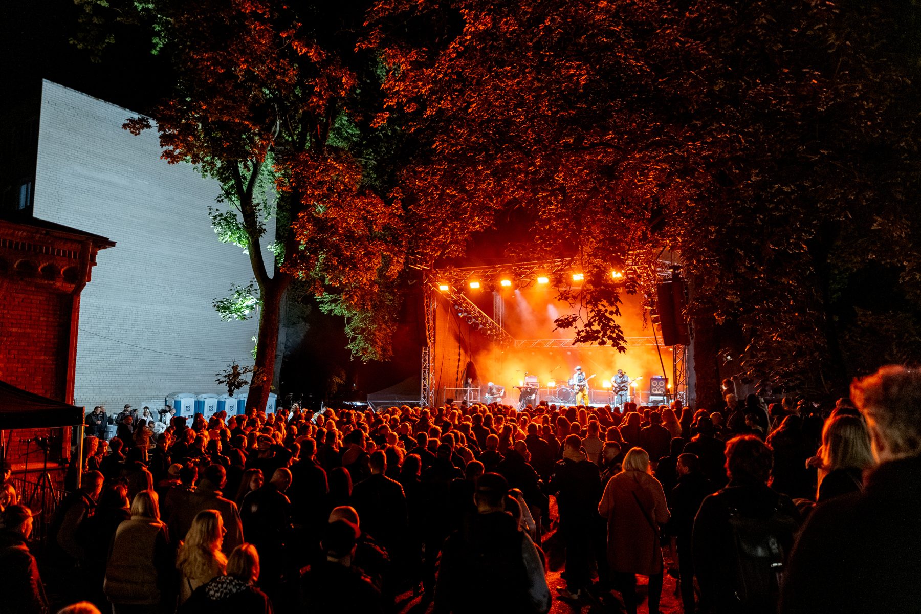 Wide view of the stage under the trees with a full crowd