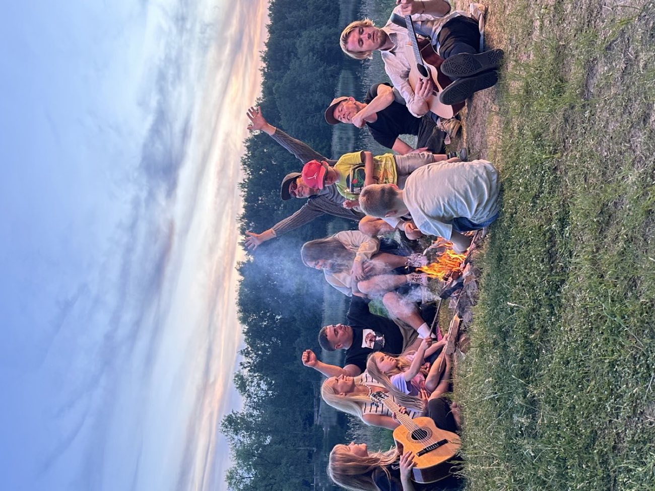 Still from the video: young people with guitars around a bonfire by a lake